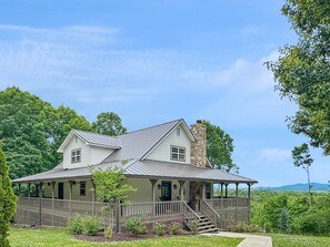 A two-story house with a porch, a chimney, and a view of the surrounding greenery.
