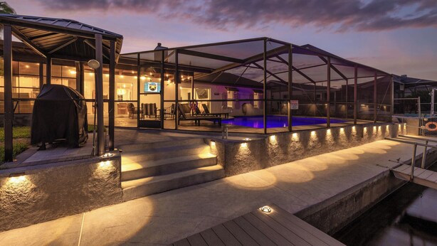 A covered outdoor swimming pool area with a patio, steps, and a grill.