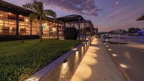 A modern building with large glass windows, a covered outdoor area, and a waterfront view.