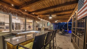 A bar area with a thatched roof, bar stools, and a view of the pool.