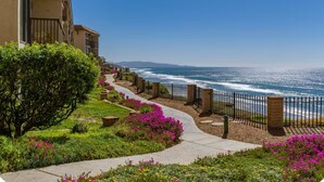 Un hotel sulla costa con un percorso che conduce alla spiaggia, immerso nel verde e tra fiori.