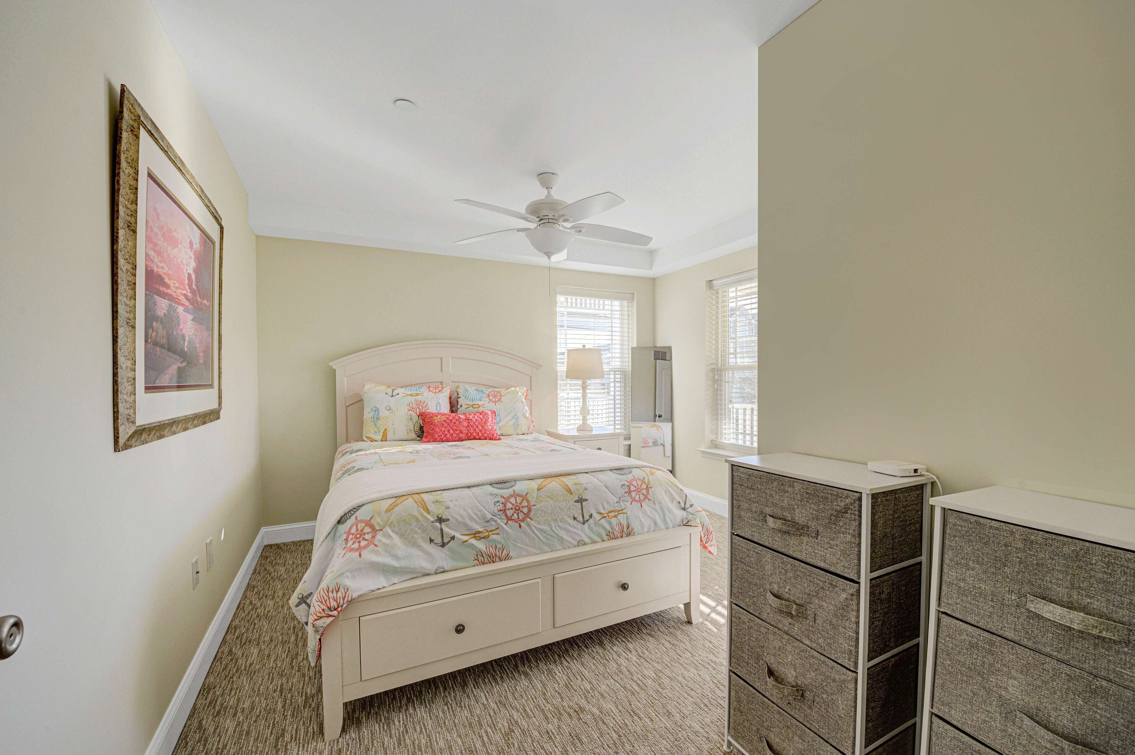 A bedroom with a bed, a dresser, a ceiling fan, and a framed picture on the wall.