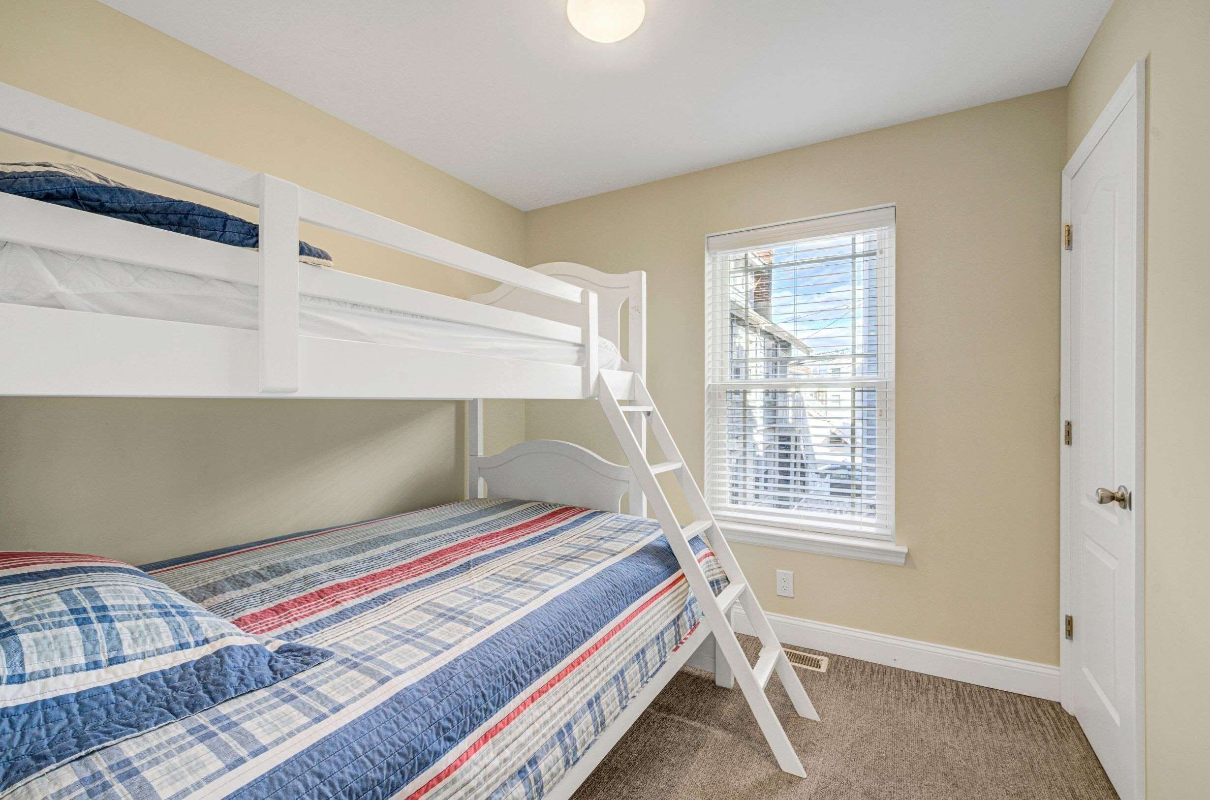 Una cama individual superpuesta con una escalera, una ventana con persianas y una puerta.