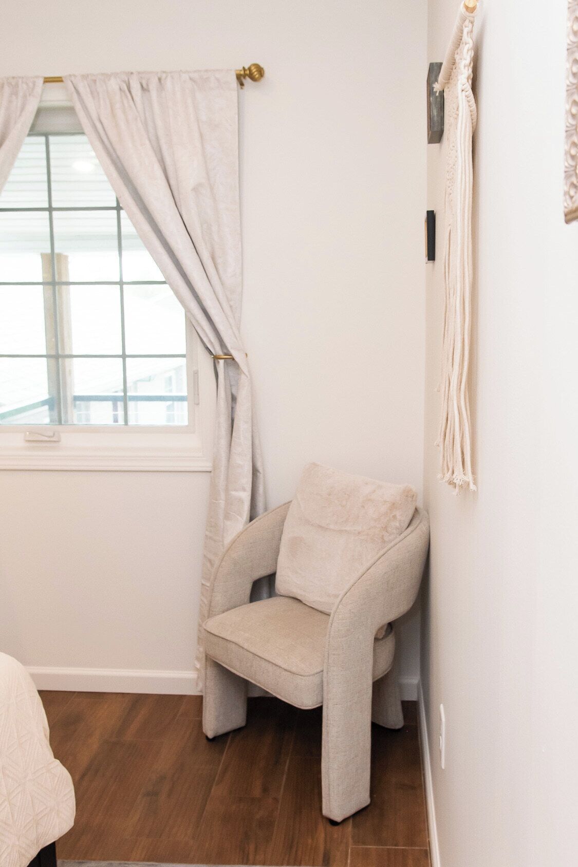 A corner room with a window, a chair, and a wall-mounted light fixture.