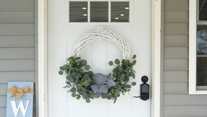 A white door with a wreath, a welcome sign, and a doormat.