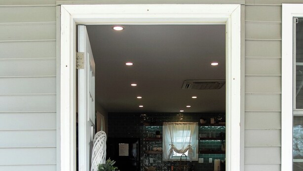A doorway leading to a dining area with a table and chairs, a rug, and a welcome sign.