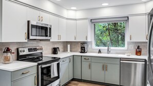 A modern kitchen with white cabinets, stainless steel appliances, and a window with a view of trees. - Inviting Red Mountain Retreat, Near Hot Springs & Downtown, Great for Families (Glenwood Springs)