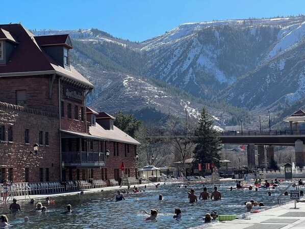 Zona de piscina con montañas al fondo, un puente y un edificio con un cartel.