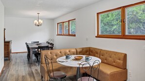 A dining area with a round table, brown cushioned bench, and chairs. There are two windows with wooden frames and a chandelier above the table. - Inviting Red Mountain Retreat, Near Hot Springs & Downtown, Great for Families (Glenwood Springs)
