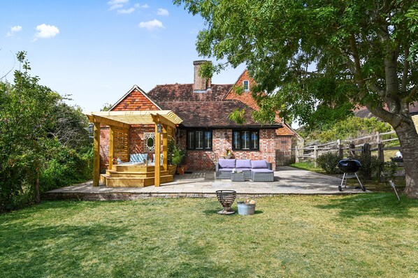 A brick house with a wooden pergola, outdoor seating, and a barbecue grill. - The Potting Shed -  a holiday let that sleeps 2 guests  in 1 bedroom (Hartfield)