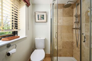 A bathroom with a toilet, a shower with a glass door, a window with blinds, and a framed picture on the wall. - The Potting Shed -  a holiday let that sleeps 2 guests  in 1 bedroom (Hartfield)