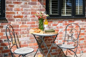 A table with a bottle of wine, a vase of flowers, and a basket of bread against a brick wall. - The Potting Shed -  a holiday let that sleeps 2 guests  in 1 bedroom (Hartfield)
