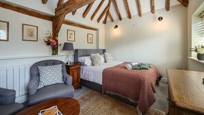 Een gezellige kamer met een bed, een grijze bank, een houten tafel en een plafond met zichtbare balken.