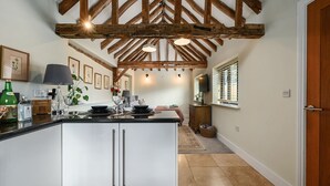 Een moderne keuken met een centraal kookeiland, houten balken in het plafond en een eethoek met een tafel en stoelen.