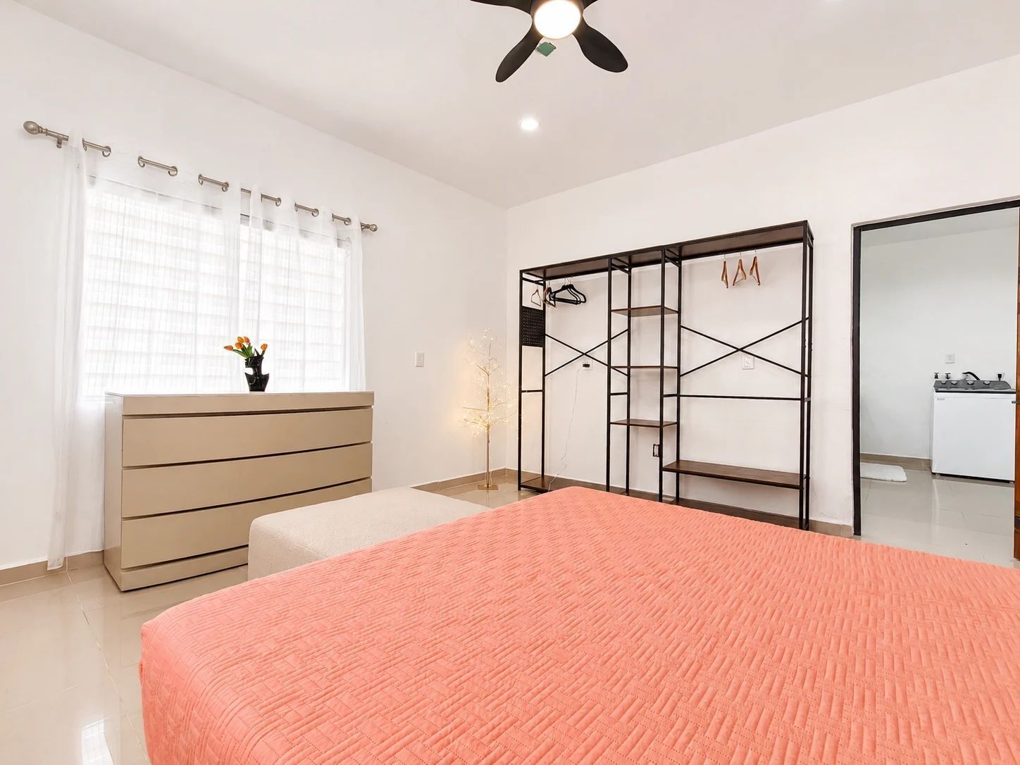 Ein Schlafzimmer mit Bett, Kommode, Kleiderschrank, Deckenventilator und einem fenster mit Vorhängen.
