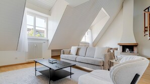A modern loft bedroom with a sloped ceiling, a built-in fireplace, a sofa, a coffee table, and a large window.