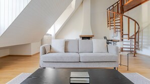 A modern loft-style living room with a high ceiling, a built-in fireplace, a grey sofa, and a wooden spiral staircase.