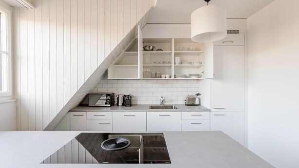 A modern kitchen with white cabinetry, a built-in stove, and a hanging light fixture.