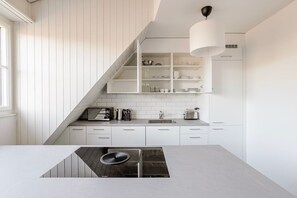 Cozinha moderna com armários brancos, fogão embutido e luminária pendente.
