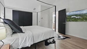 Een slaapkamer met een bed, een zwart-wit koeienhuid tapijt, een televisie aan de muur en een deur naar een andere kamer.