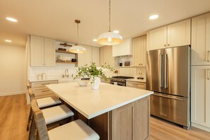 Una cocina moderna con una isla grande, electrodomésticos de acero inoxidable e iluminación colgante.
