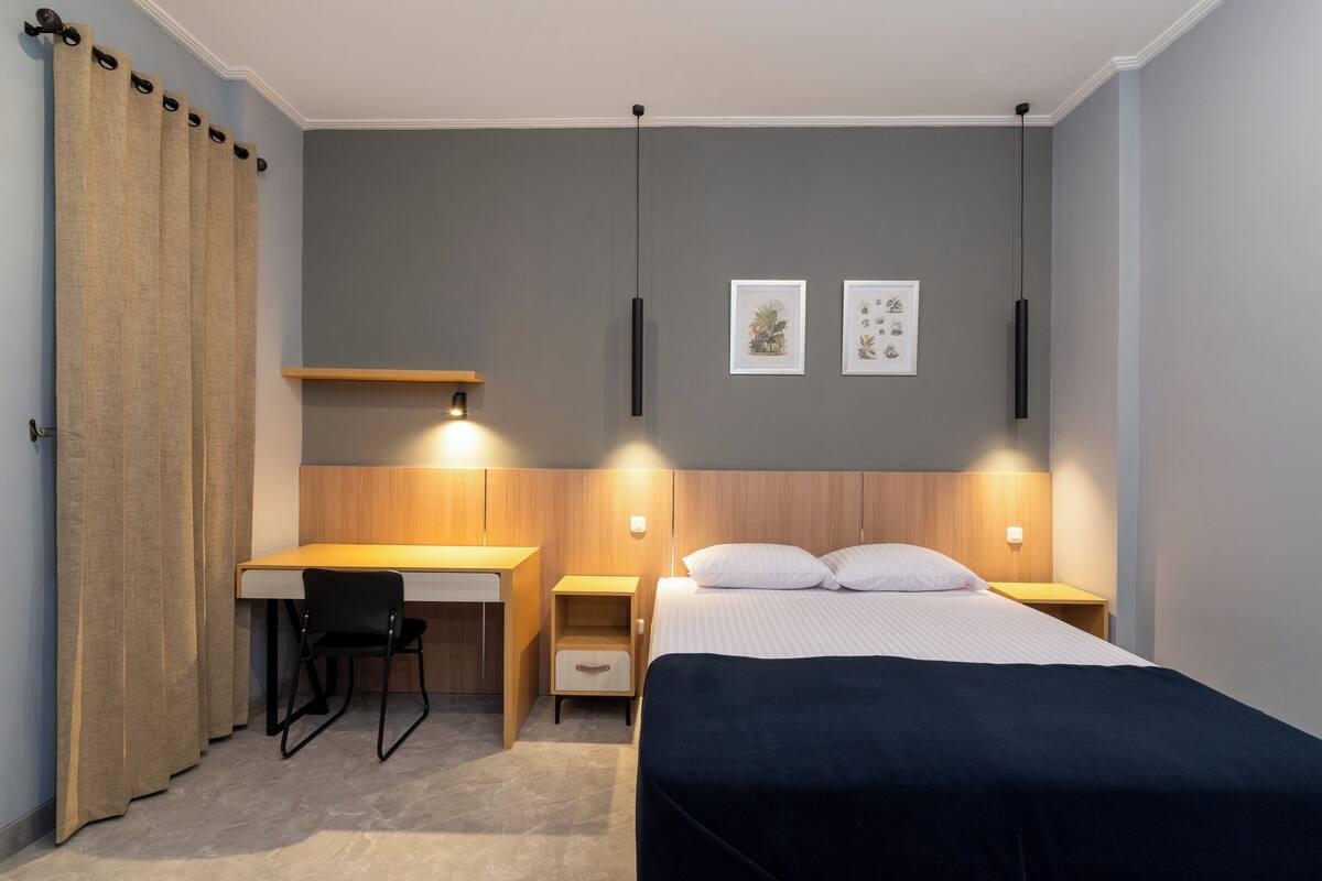 Una habitación de hotel moderna con cama, escritorio, silla y dos mesitas de noche.