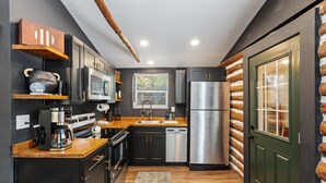 A modern kitchen with dark cabinetry, stainless steel appliances, and a wooden countertop.