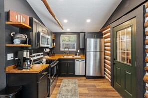 A modern kitchen with dark cabinetry, stainless steel appliances, and a wooden countertop.