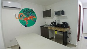 A small kitchenette with a microwave, stove, and sink. There is a colorful mural on the wall and a white table. - Villa Leo Beautiful room with shared kitchenette, in the heart of Cancun (Cancun)