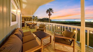 Eine überdachte Terrasse mit Sitzgelegenheiten, einem Tisch und Blick auf den Sonnenuntergang über dem Meer.