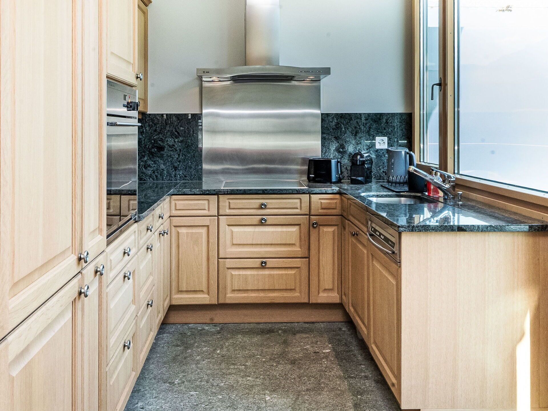 Une cuisine de taille réduite, dotée de meubles en bois, d’une cuisinière en acier inoxydable et d’une fenêtre offrant une vue agréable.