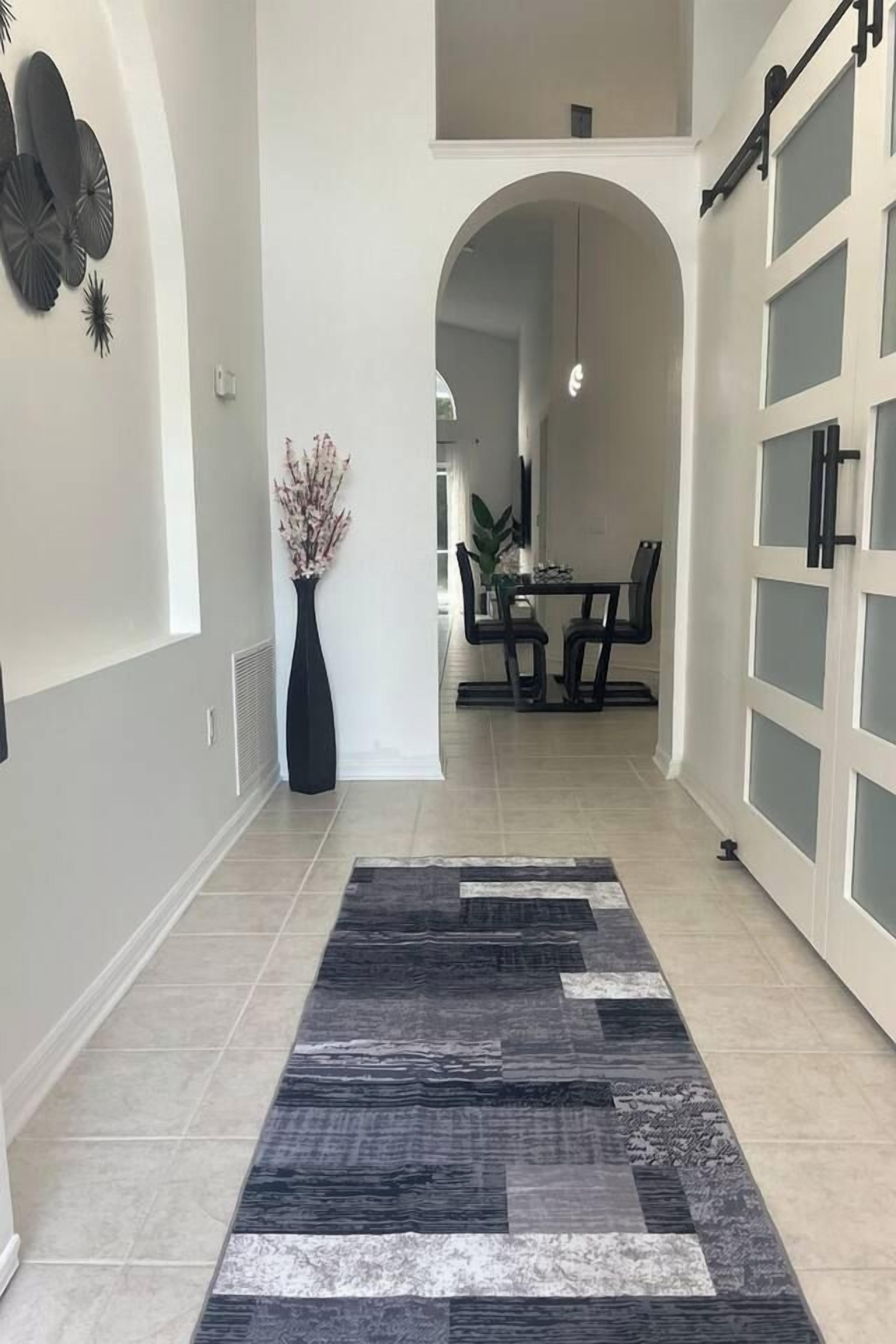 A hallway with a patterned rug, a vase with flowers, and a dining area with chairs and a table.