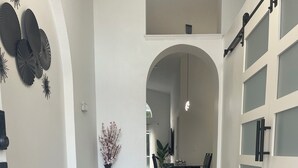 Un pasillo con un tapete estampado, un comedor con mesa y sillas, y una puerta corredera con paneles de vidrio esmerilado.