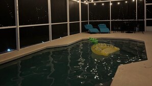 Un área de piscina con paredes de vidrio transparente, luces colgantes y sillas azules.