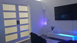 Una sala de estar moderna con ventilador de techo, televisor de pantalla plana montado en la pared y puerta corrediza de vidrio.