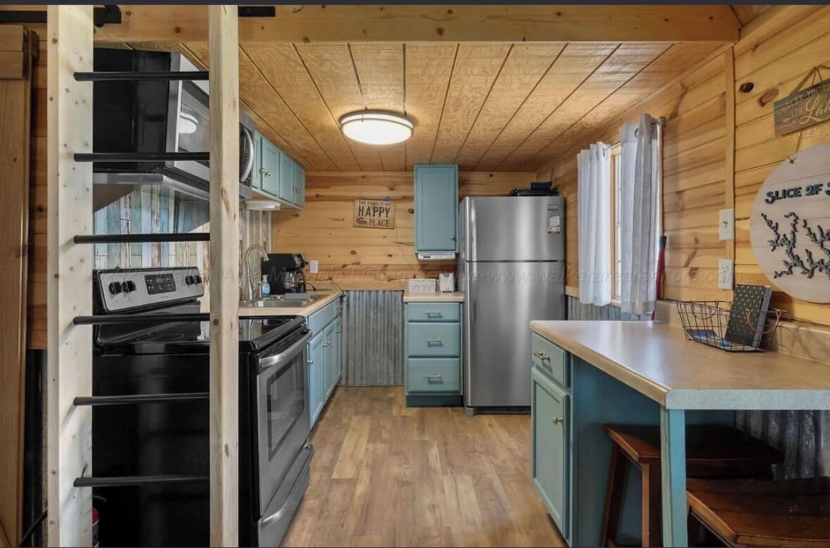 Una cocina compacta con paredes de madera, un refrigerador de acero inoxidable y un horno empotrado.