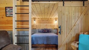 A cozy wooden cabin interior with a bed, a chair, and a small table.