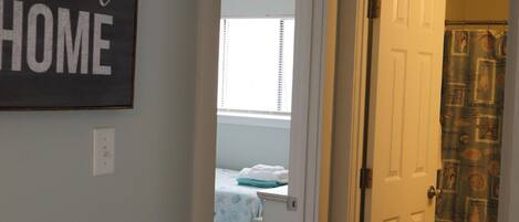A hallway with a sign that reads "HOME is sweet HOME," leading to a bedroom with a bed and a window.