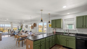 A modern kitchen with green cabinets, a large island, and a dining area with a view. - Amazing Mountain Views  (Lake Placid)