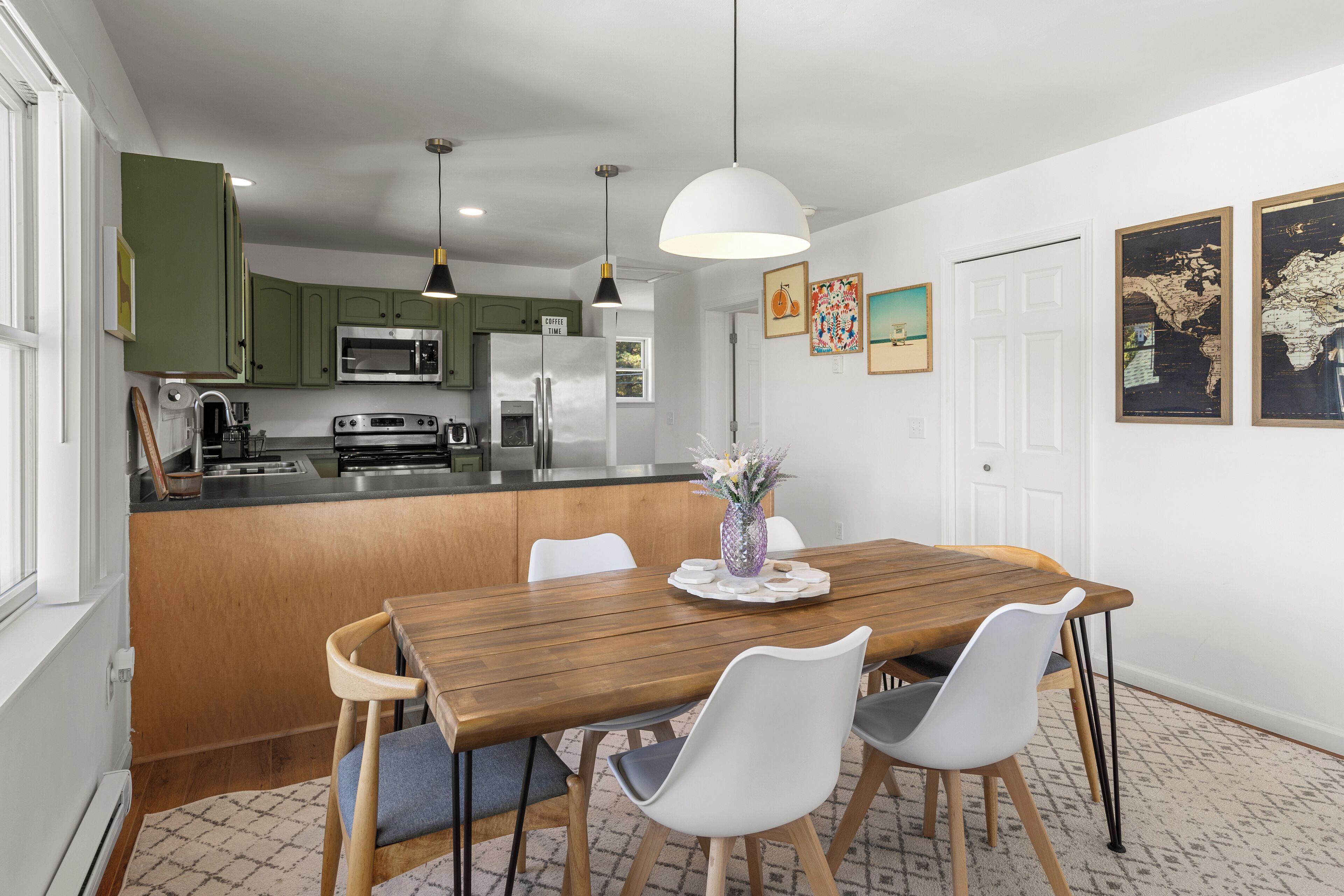 Una cocina moderna con armarios verdes, una mesa de comedor de madera y sillas blancas.