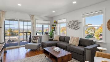 A spacious living room with a gray sectional sofa, a wooden coffee table, and a view of the outdoors through large windows.