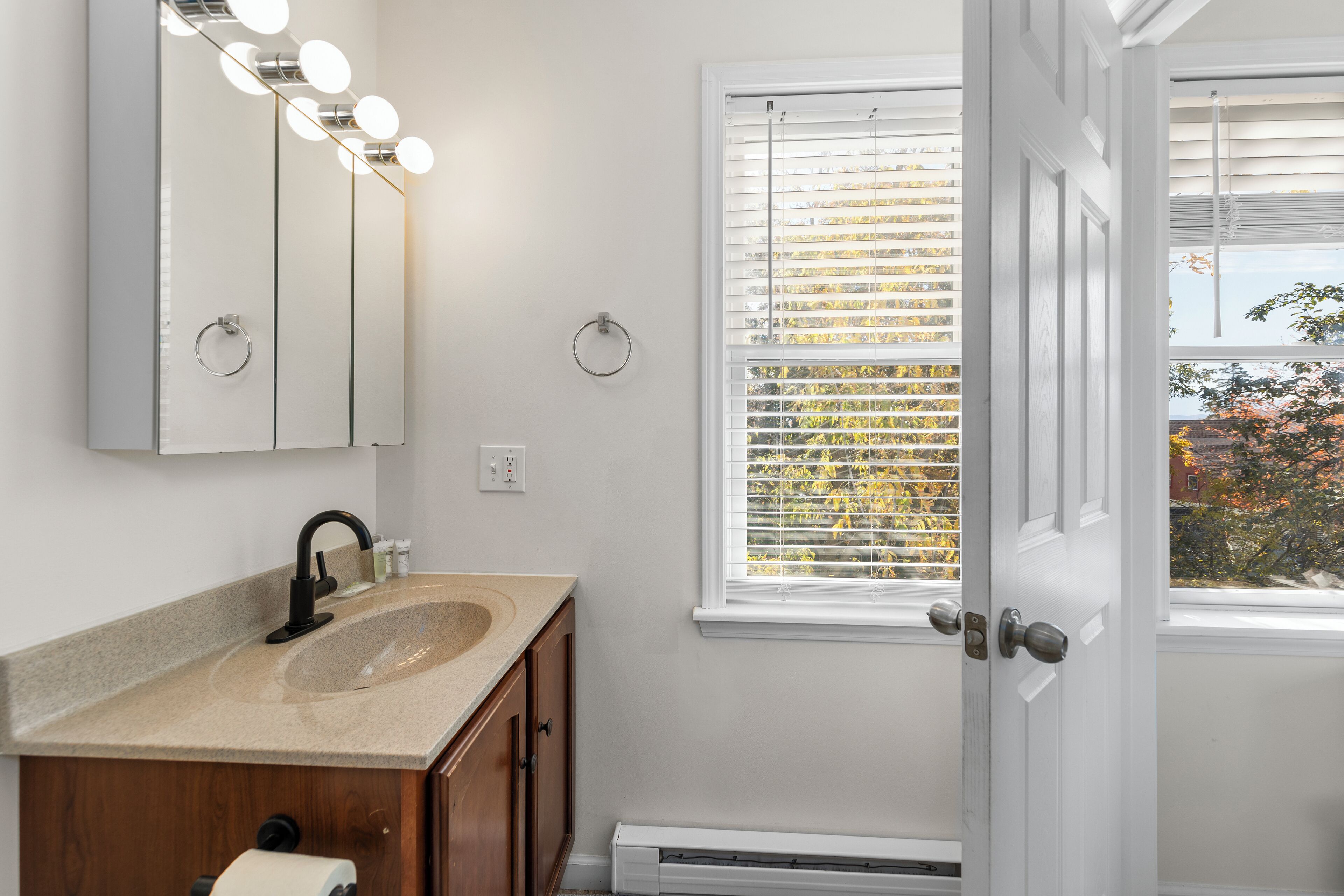 A bathroom with a sink, mirror, and window with blinds.