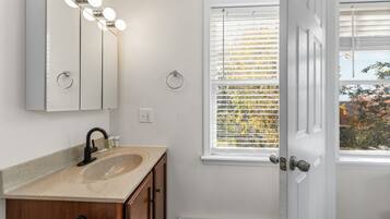 A bathroom with a sink, mirror, and window with blinds.