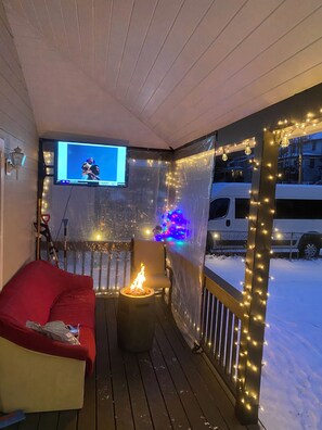 A covered outdoor area with a TV screen, a fire pit, and string lights. - Amazing Mountain Views  (Lake Placid)