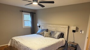 A bedroom with a bed, a ceiling fan, a nightstand, and a window.