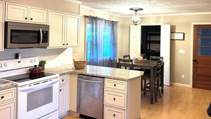 A kitchen with white cabinets, a stainless steel microwave, a stove, and a dishwasher. There is a dining area with a table and chairs.