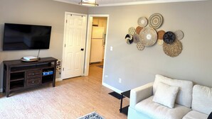 A living room with a flat-screen TV, a dark wooden entertainment center, a beige sofa, and a wall-mounted decorative item.