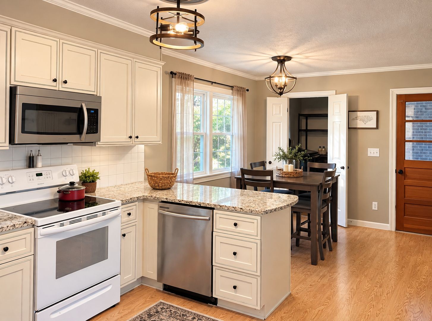A kitchen with white cabinetry, a stainless steel microwave, a red pot on the stove, and a wooden dining table with chairs.
