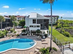 A modern building with a pool, surrounded by palm trees and a view of the ocean. - Coming Soon Cyprina 2 Direct Water Views (Sanibel)