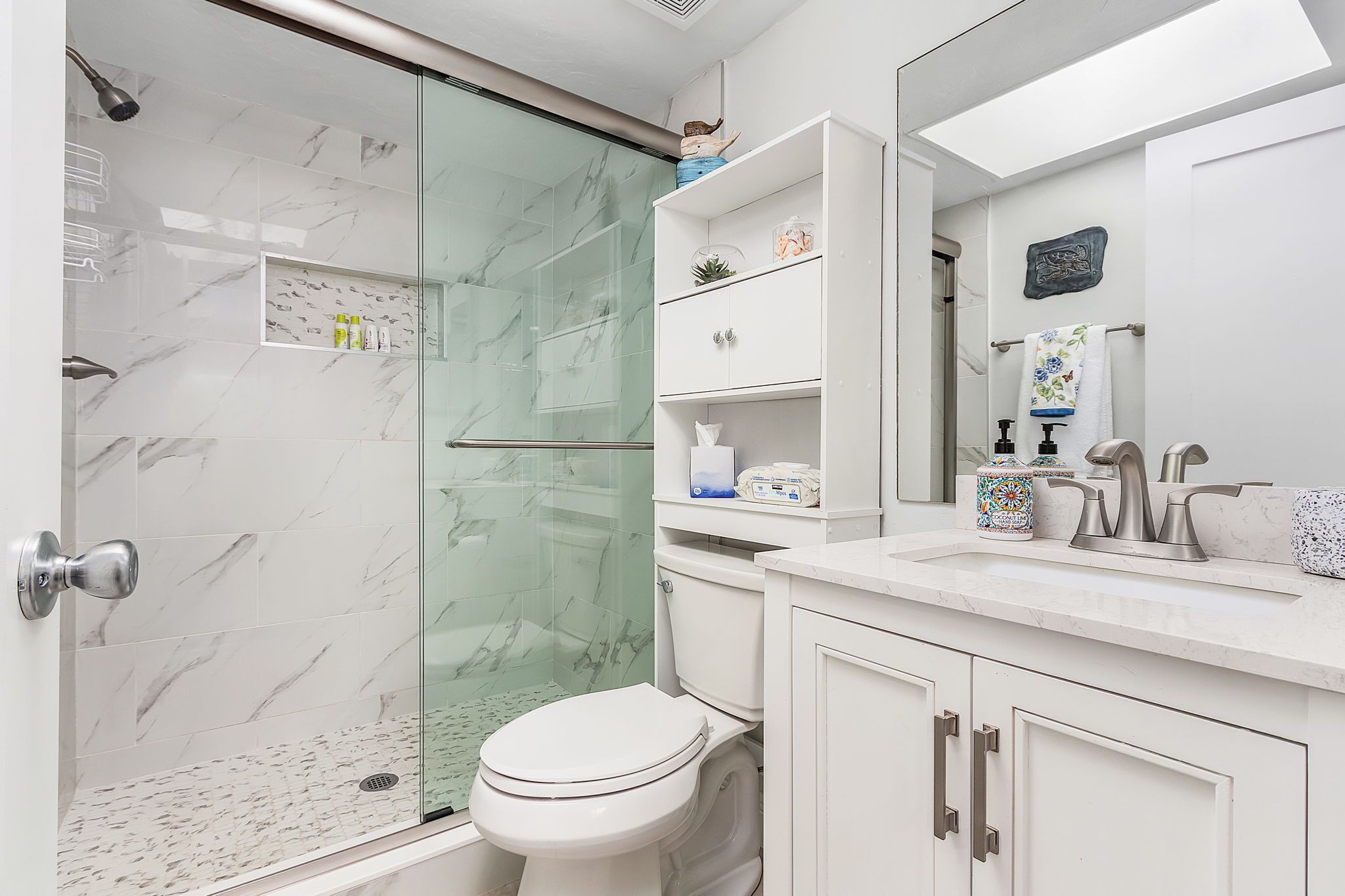 Un baño moderno con ducha de vidrio, inodoro blanco y tocador con lavamanos y espejo.